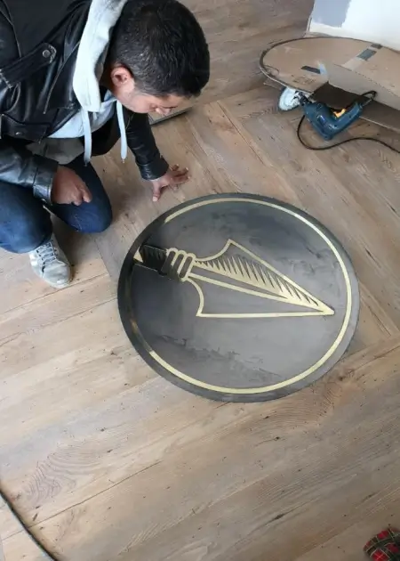 arafed man painting a large metal plate with a gold arrow