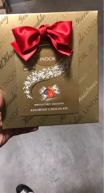 someone holding a box of chocolate with a red bow on it